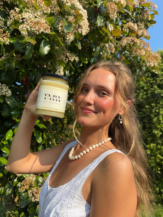 lady holding up a jar of original moss gel outside in the sun in front of a hedge